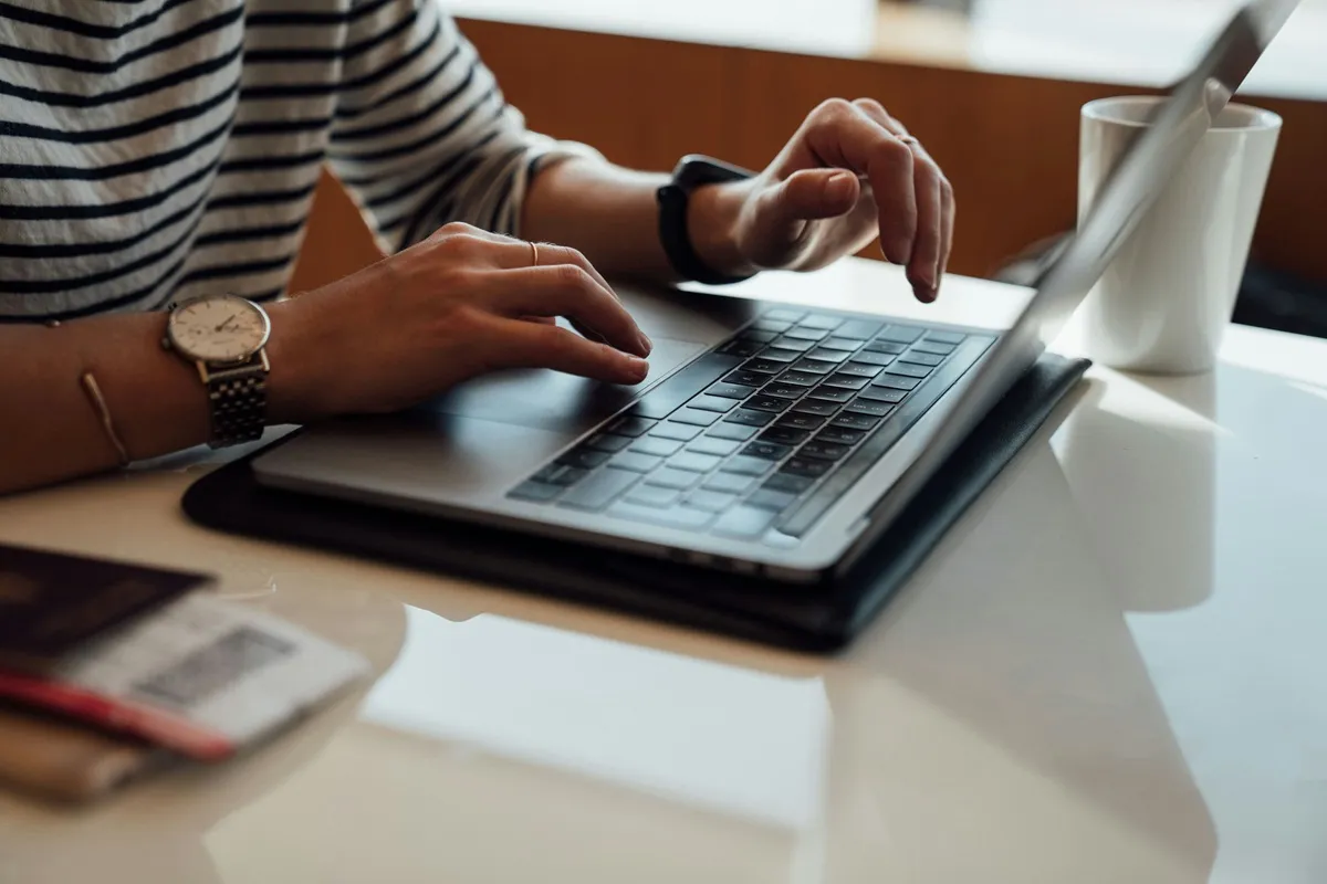 Pessoa digitando em um notebook com uma xícara de café ao lado