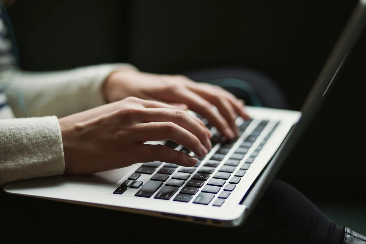 Mãos femininas digitando em um teclado de laptop, representando concentração e produtividade no ambiente de trabalho ou estudos.