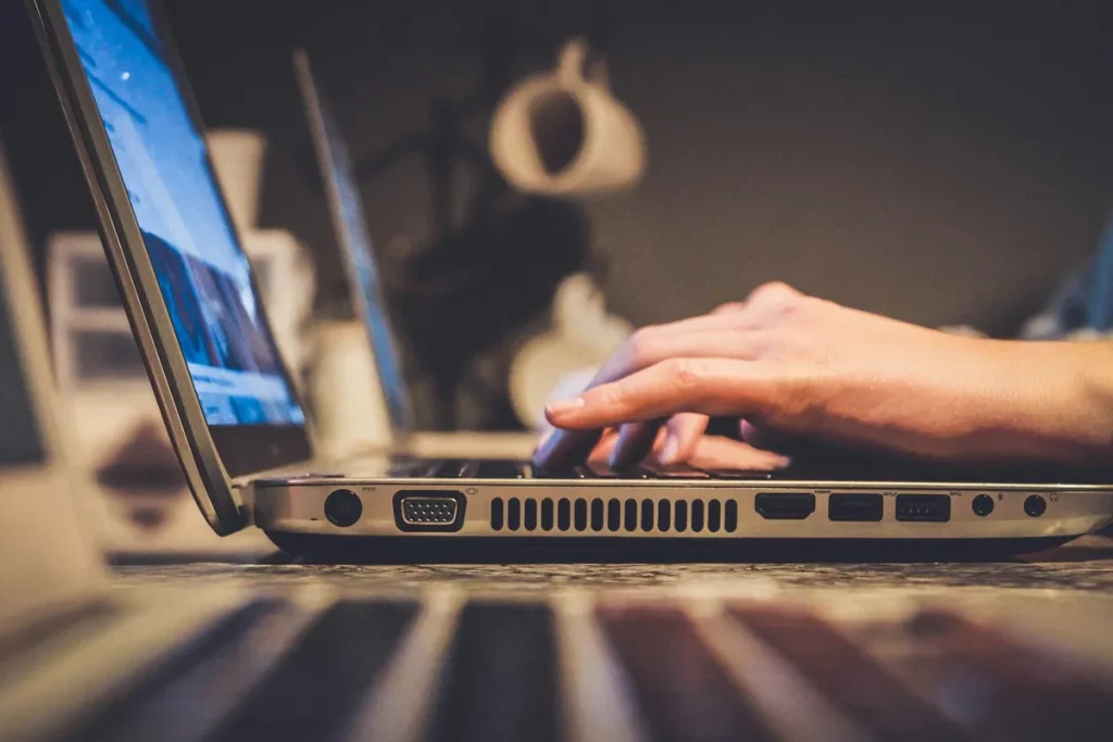 Mãos digitando em um laptop com foco lateral, destacando a conectividade e o trabalho digital.