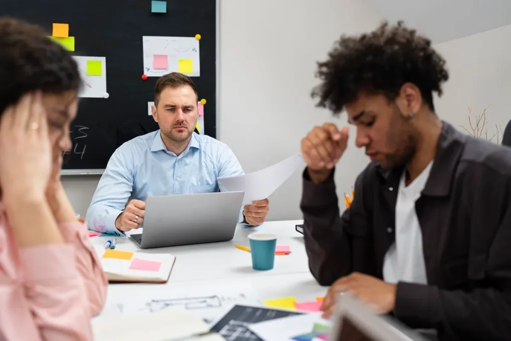 Equipe de trabalho em reunião com expressões sérias, analisando documentos e estratégias em um escritório.