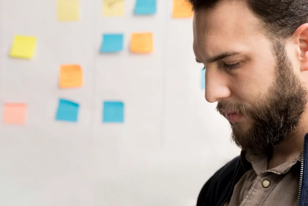 Homem com barba observando post-its coloridos em um quadro branco durante um processo de planejamento