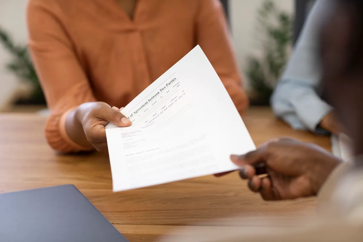 Pessoa entregando um documento impresso em um ambiente corporativo, representando uma carta de desligamento ou contrato formal.