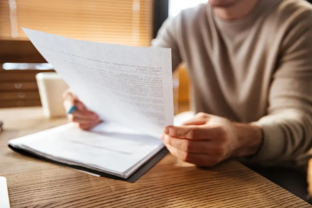 Homem segurando e lendo um documento impresso em um ambiente de escritório, representando uma carta de desligamento ou contrato.